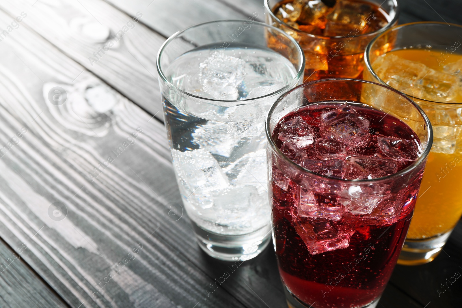 Photo of Refreshing soda water of different flavors with ice cubes in glasses on black wooden table, closeup. Space for text