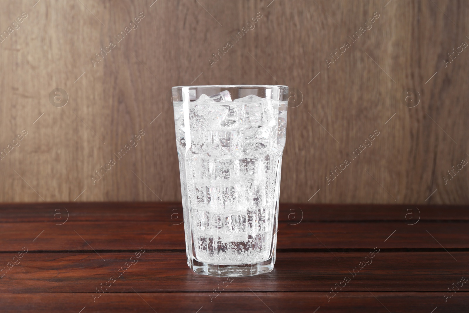 Photo of Refreshing soda water with ice cubes in glass on wooden table