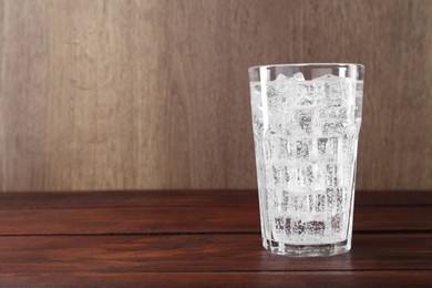 Photo of Refreshing soda water with ice cubes in glass on wooden table, space for text