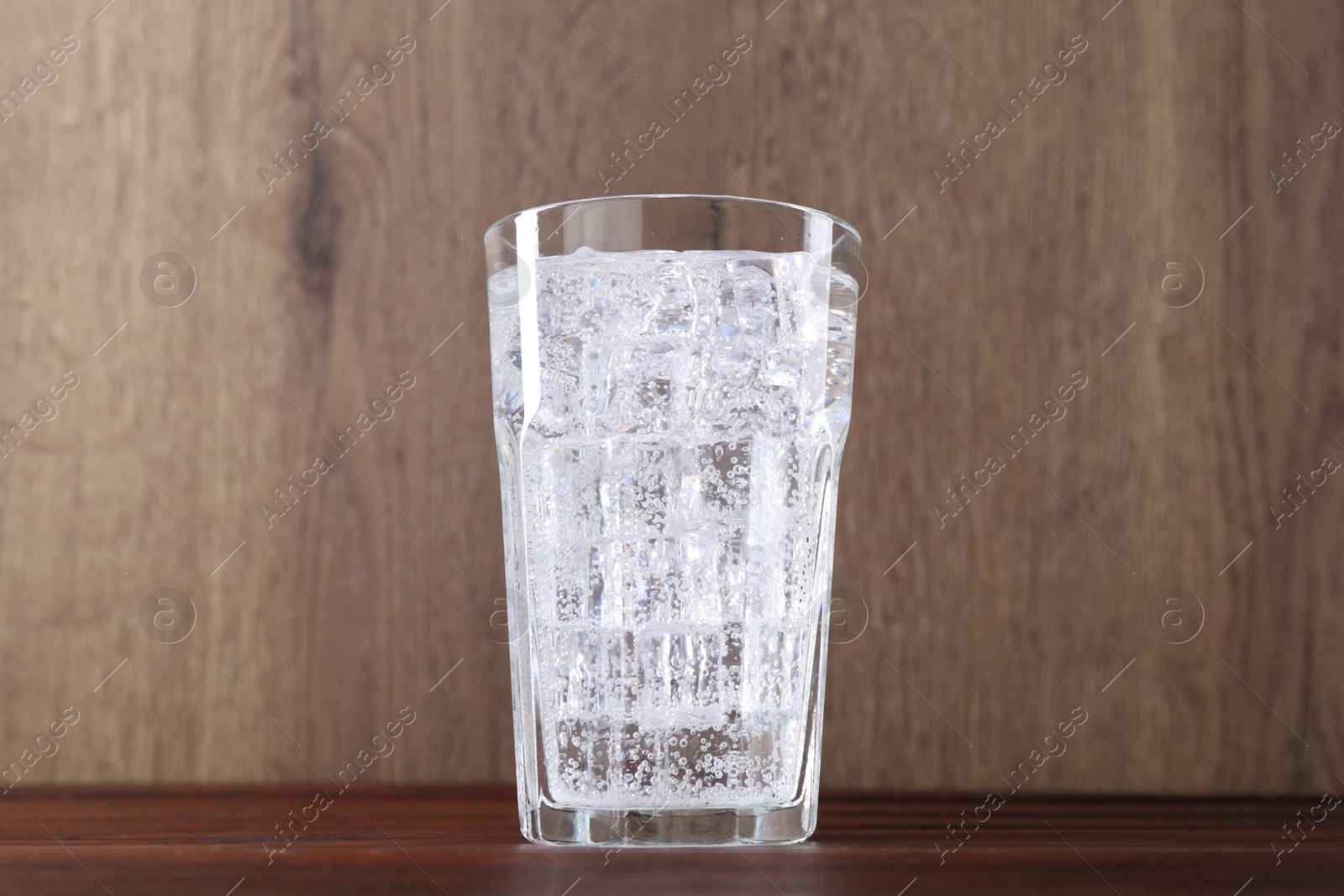 Photo of Refreshing soda water with ice cubes in glass on wooden table