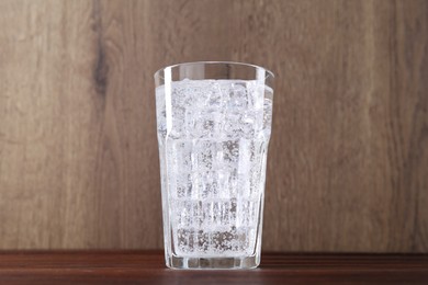 Photo of Refreshing soda water with ice cubes in glass on wooden table