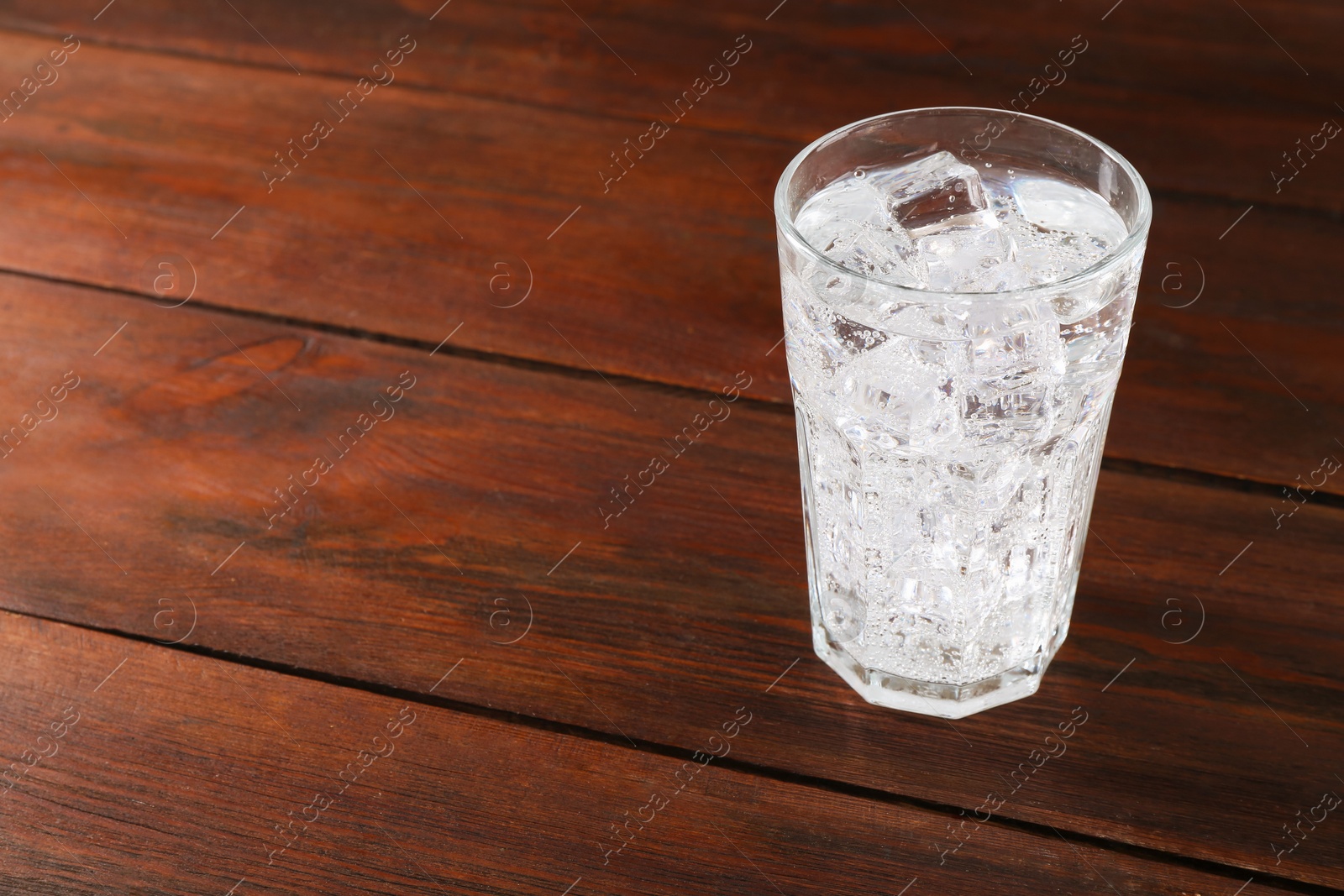 Photo of Refreshing soda water with ice cubes in glass on wooden table, space for text