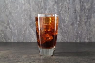 Photo of Sweet soda water with ice cubes in glass on grey table