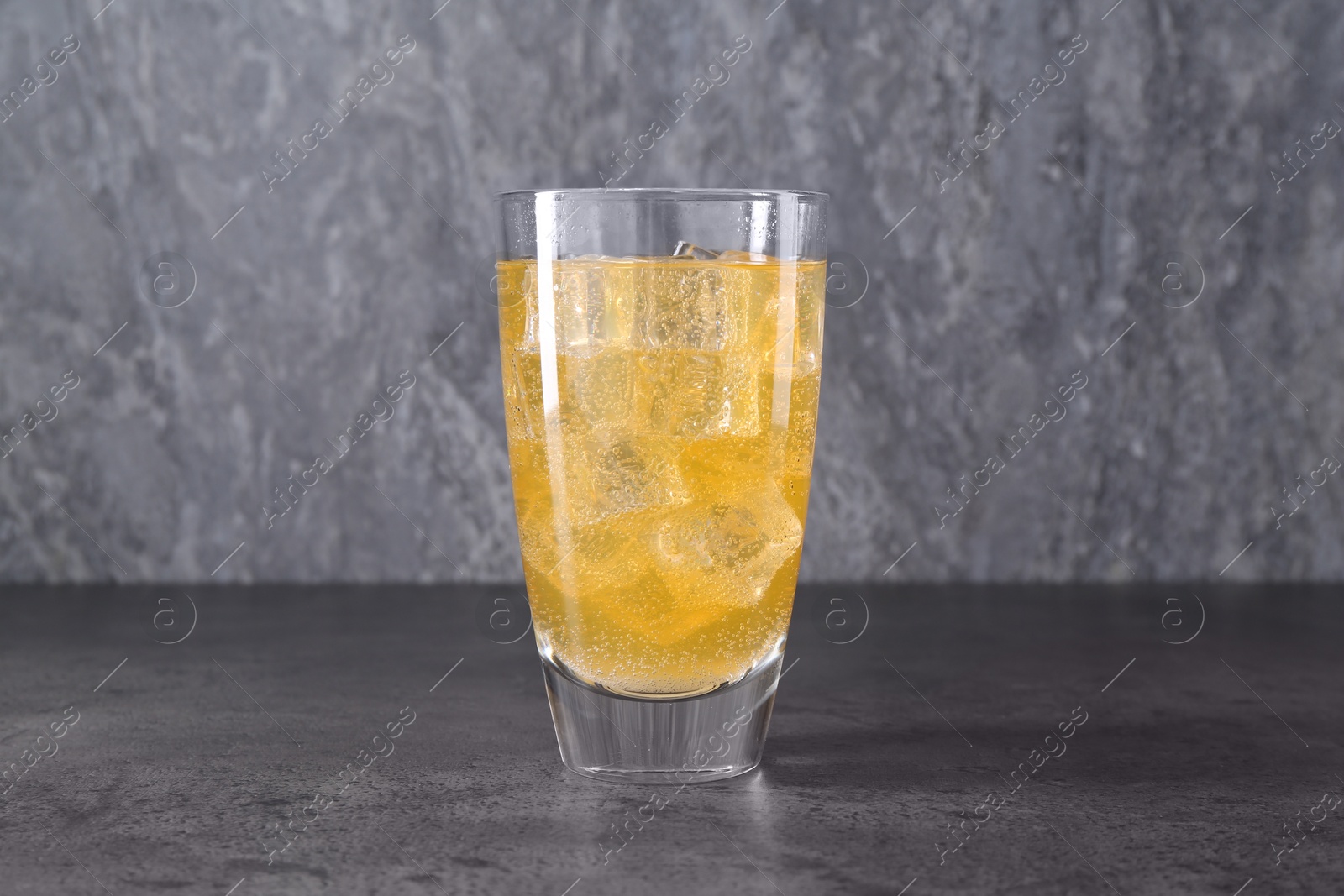 Photo of Sweet soda water with ice cubes in glass on grey table