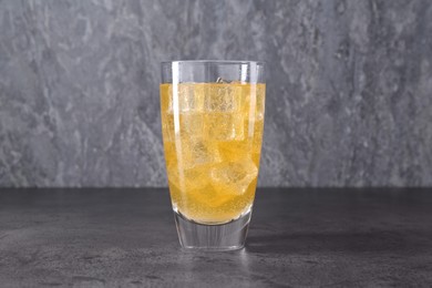 Photo of Sweet soda water with ice cubes in glass on grey table