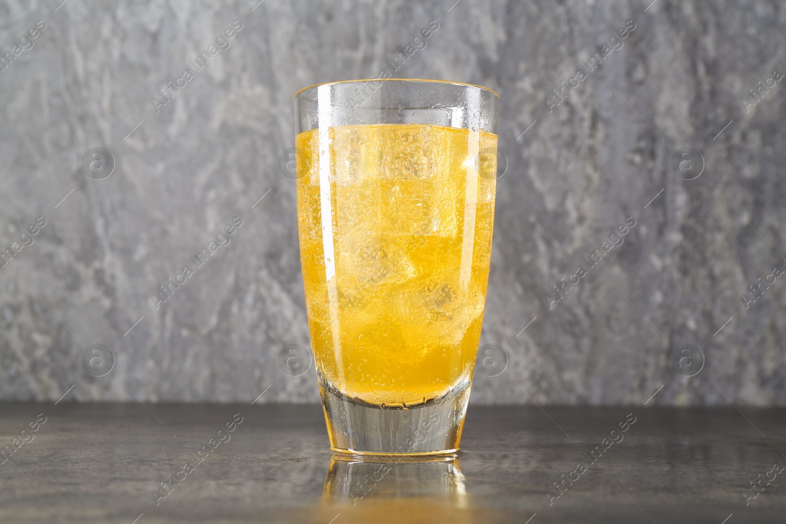 Photo of Sweet soda water with ice cubes in glass on grey table, closeup