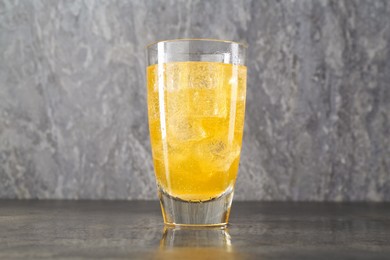 Photo of Sweet soda water with ice cubes in glass on grey table, closeup