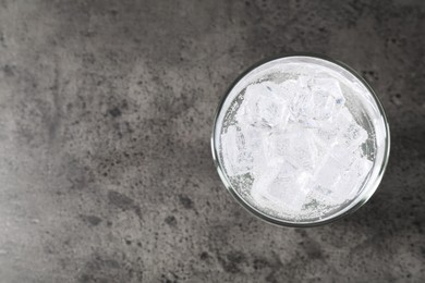 Photo of Refreshing soda water with ice cubes in glass on grey table, top view. Space for text