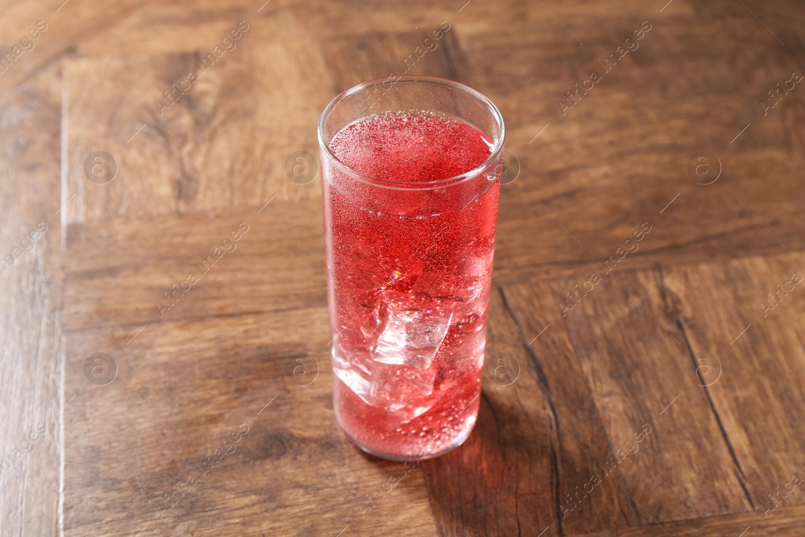 Photo of Sweet soda water with ice cubes in glass on wooden table