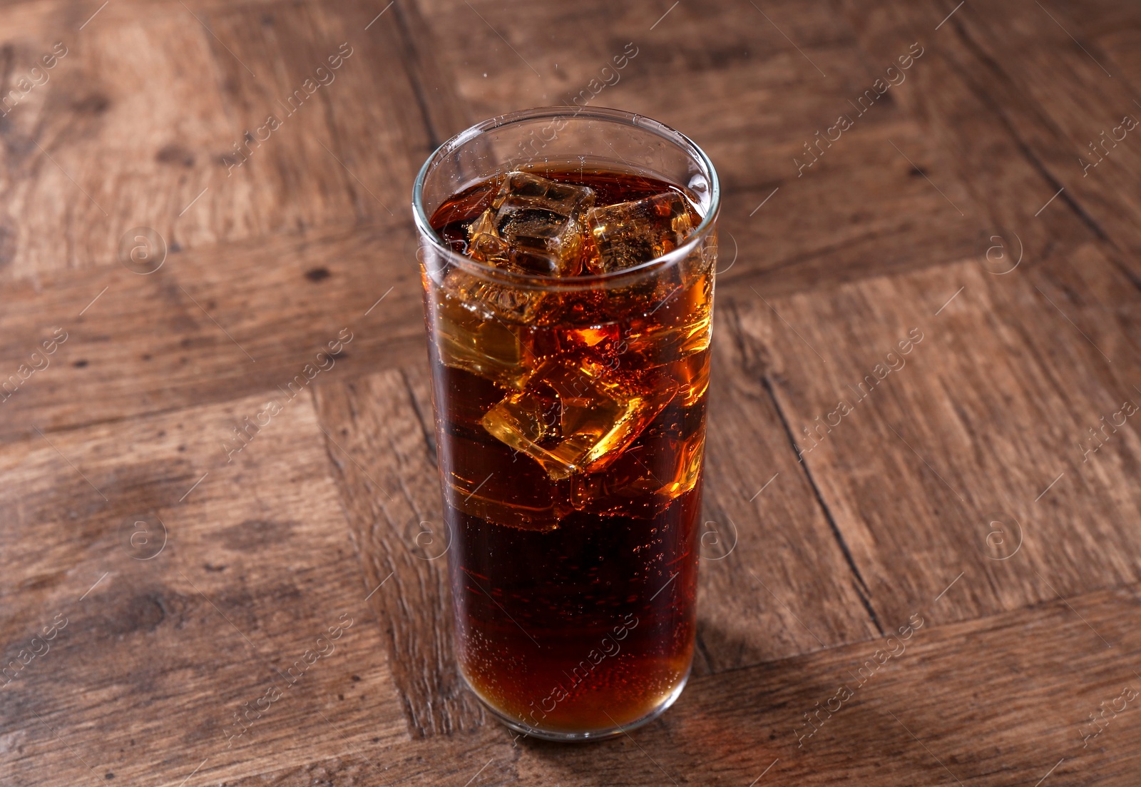 Photo of Sweet soda water with ice cubes in glass on wooden table