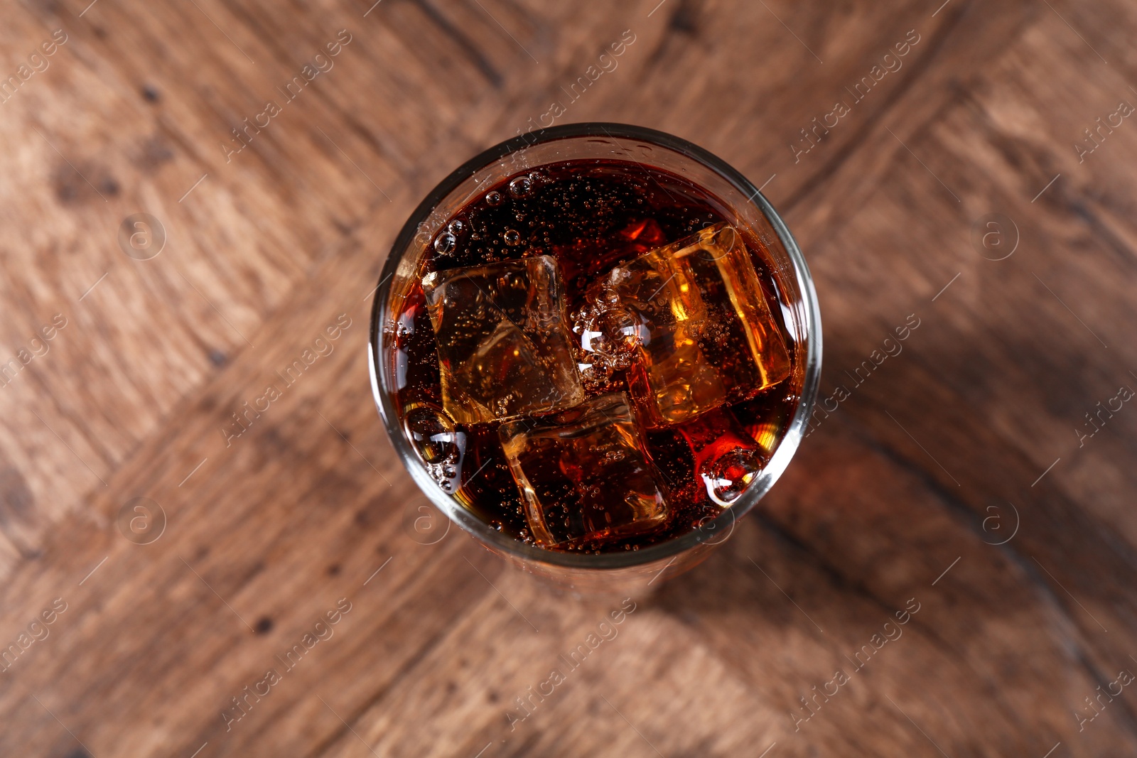 Sweet soda water with ice cubes in glass on wooden table, top view Photo of Sweet soda water with ice cubes in glass on wooden table, top view
