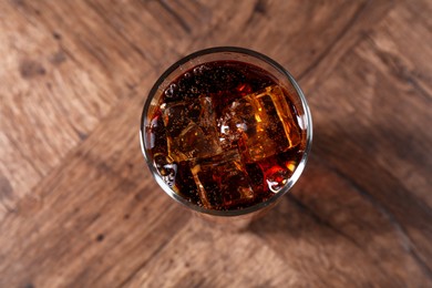 Photo of Sweet soda water with ice cubes in glass on wooden table, top view