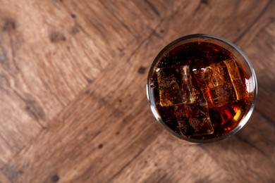 Photo of Sweet soda water with ice cubes in glass on wooden table, top view. Space for text