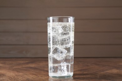 Photo of Refreshing soda water with ice cubes in glass on wooden table