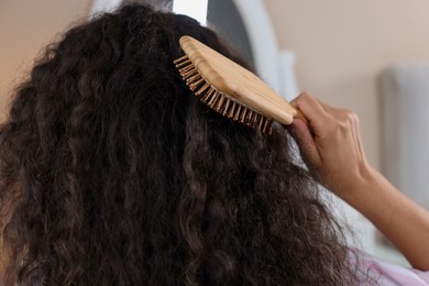 Woman brushing her curly hair indoors, closeup