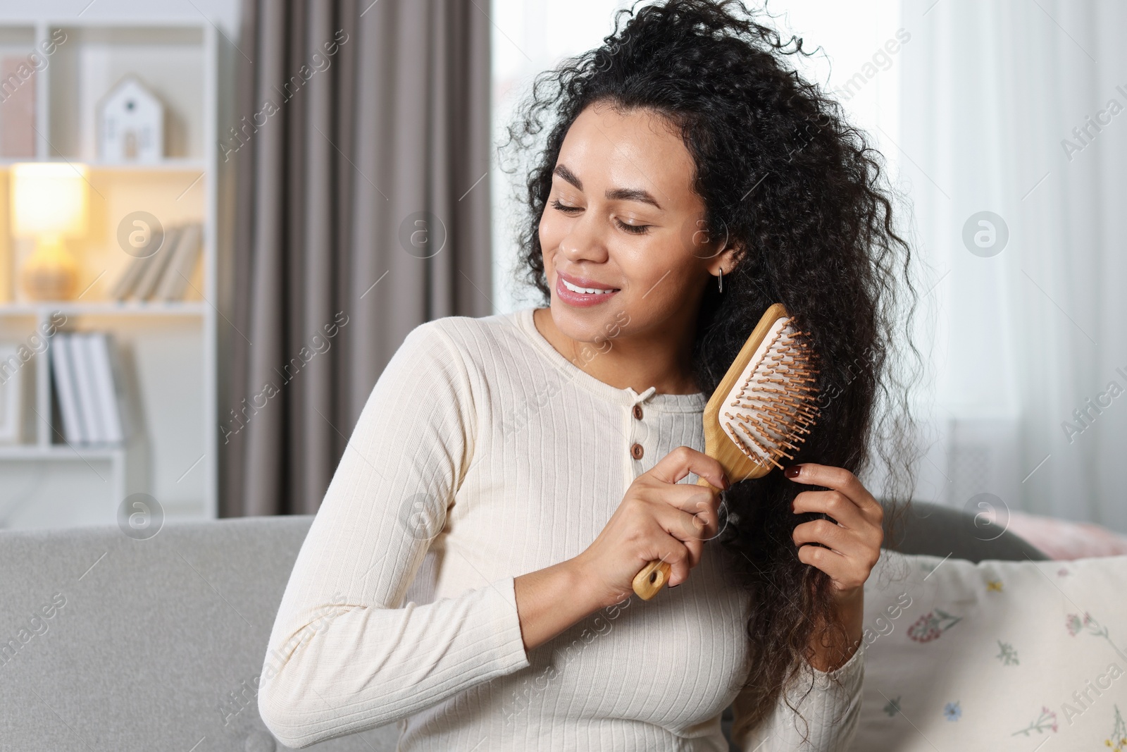 Photo of Smiling young woman brushing her curly hair at home