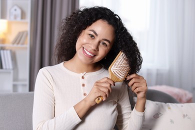 Photo of Smiling young woman brushing her curly hair at home