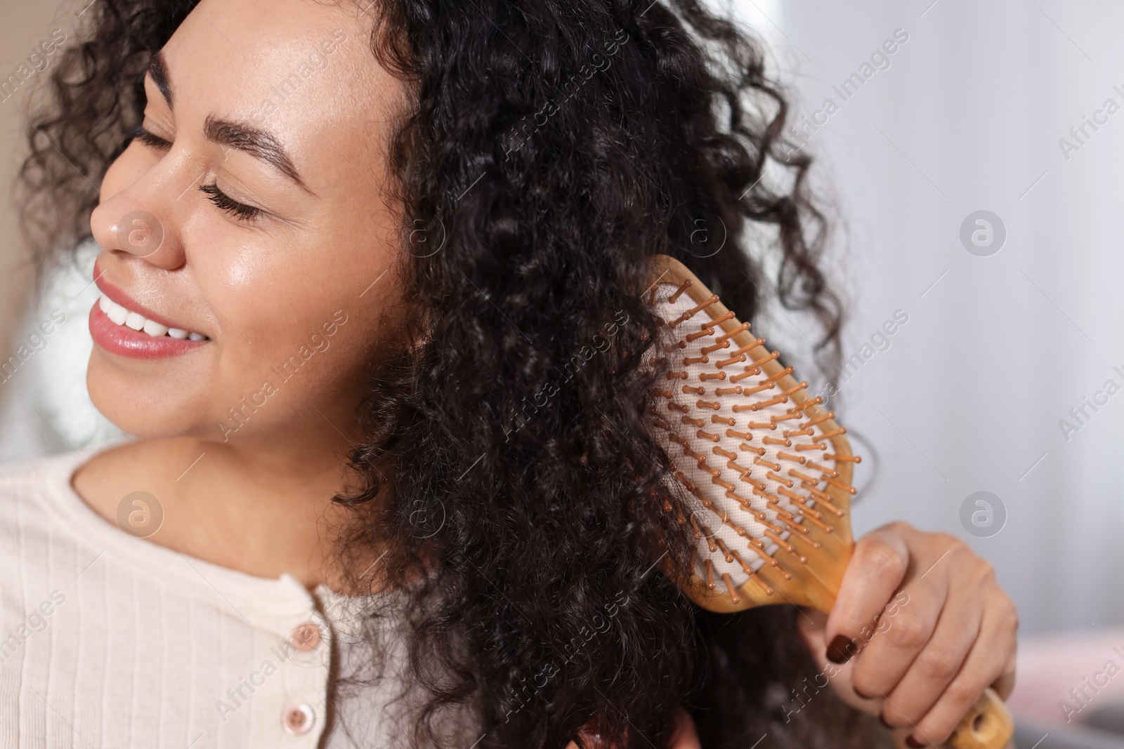 Photo of Smiling young woman brushing her curly hair indoors, closeup