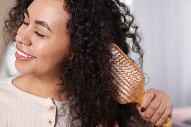 Photo of Smiling young woman brushing her curly hair indoors, closeup