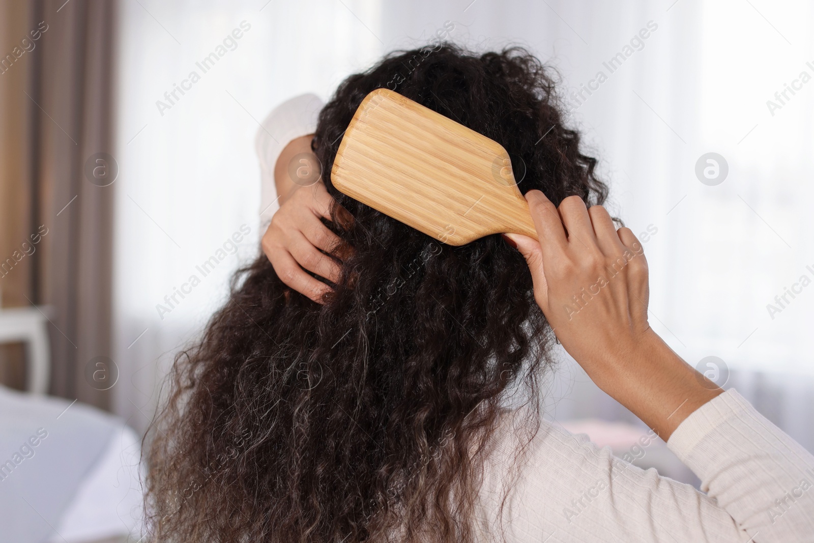 Photo of Woman brushing her curly hair at home