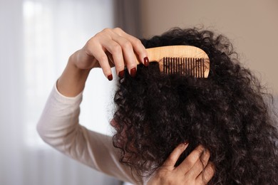 Photo of Woman brushing her curly hair with comb indoors