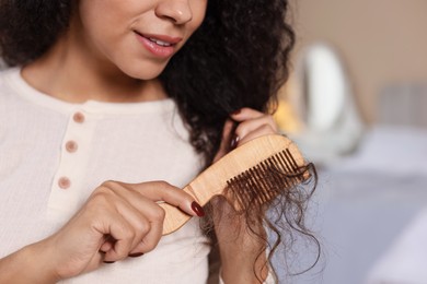 Photo of Woman brushing her curly hair with comb indoors, closeup