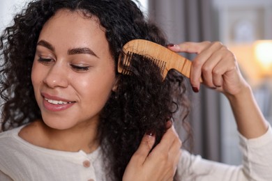 Smiling young woman brushing her curly hair with comb at home