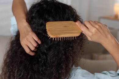 Photo of Woman brushing her curly hair indoors, closeup