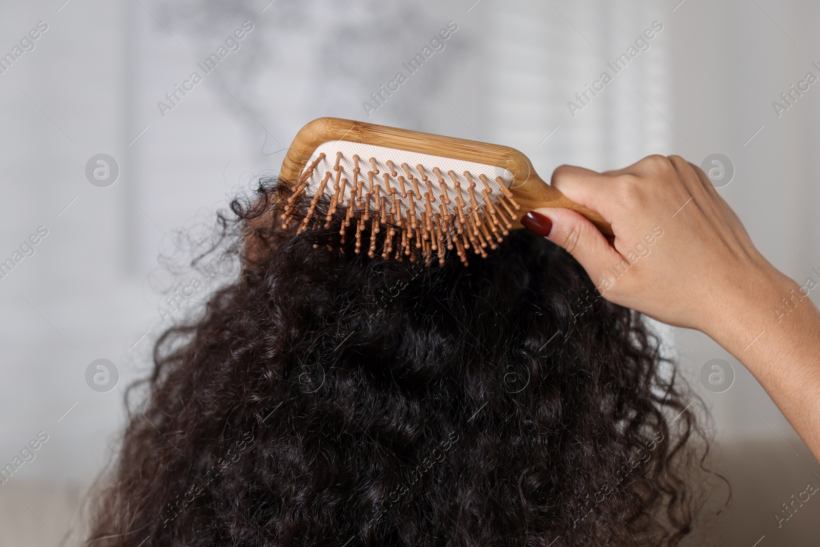 Photo of Woman brushing her curly hair indoors, closeup