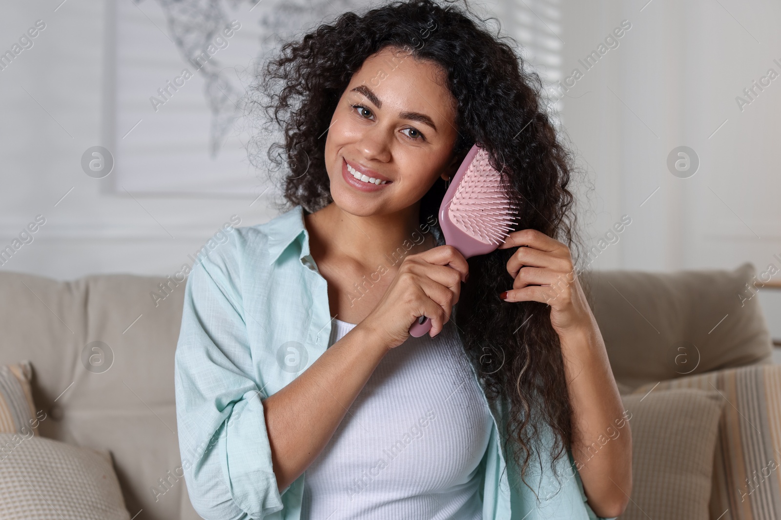 Photo of Smiling young woman brushing her curly hair at home