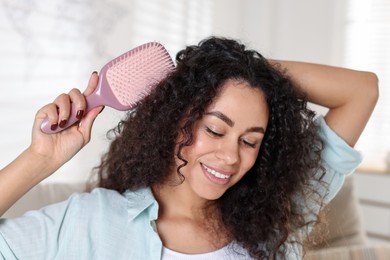 Photo of Smiling young woman brushing her curly hair at home