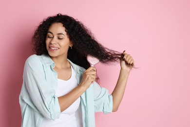 Photo of Smiling young woman brushing her curly hair on pink background