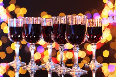 Photo of Tasty red wine in glasses on mirror surface against dark background with blurred lights, bokeh effect