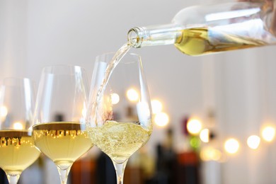 Photo of Pouring white wine into glass against blurred background with festive lights, closeup. Bokeh effect