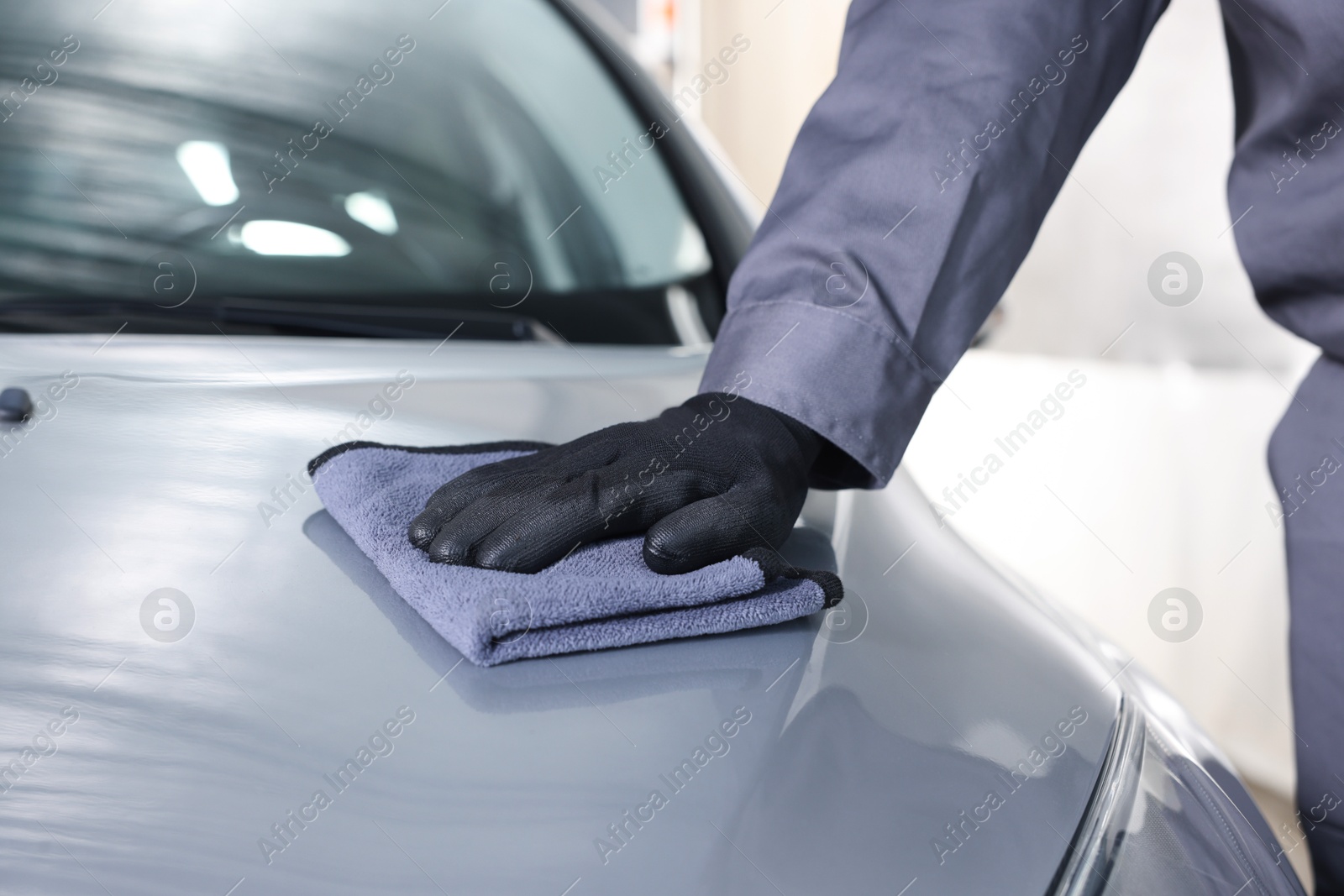 Photo of Man polishing car hood with rag indoors, closeup