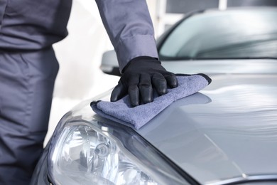 Photo of Man polishing car hood with rag indoors, closeup