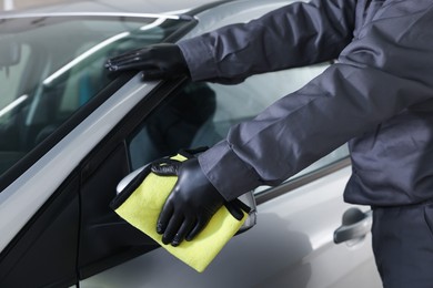 Photo of Man cleaning car side view mirror with yellow rag indoors, closeup