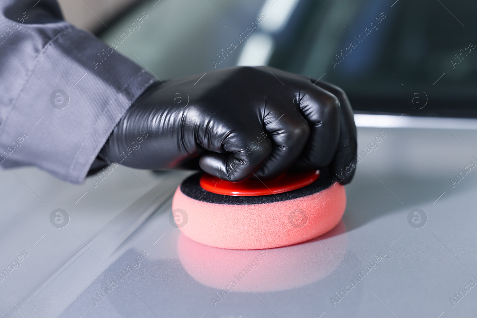 Photo of Man polishing car hood with sponge indoors, closeup