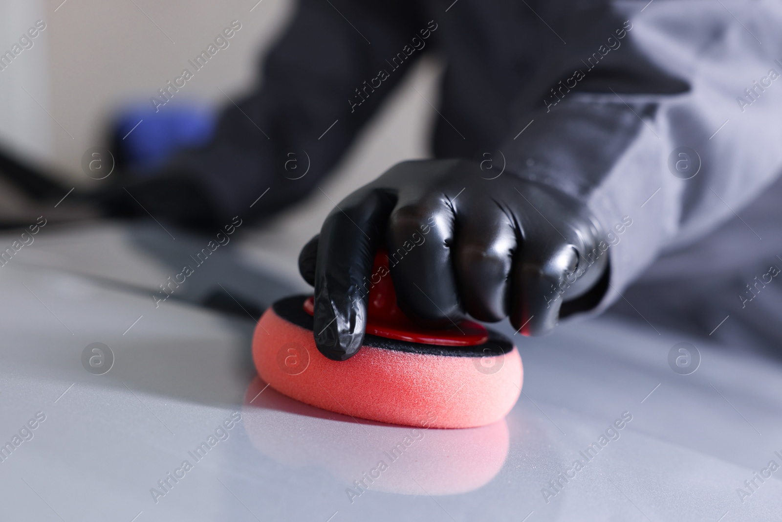 Photo of Man polishing car hood with sponge indoors, closeup