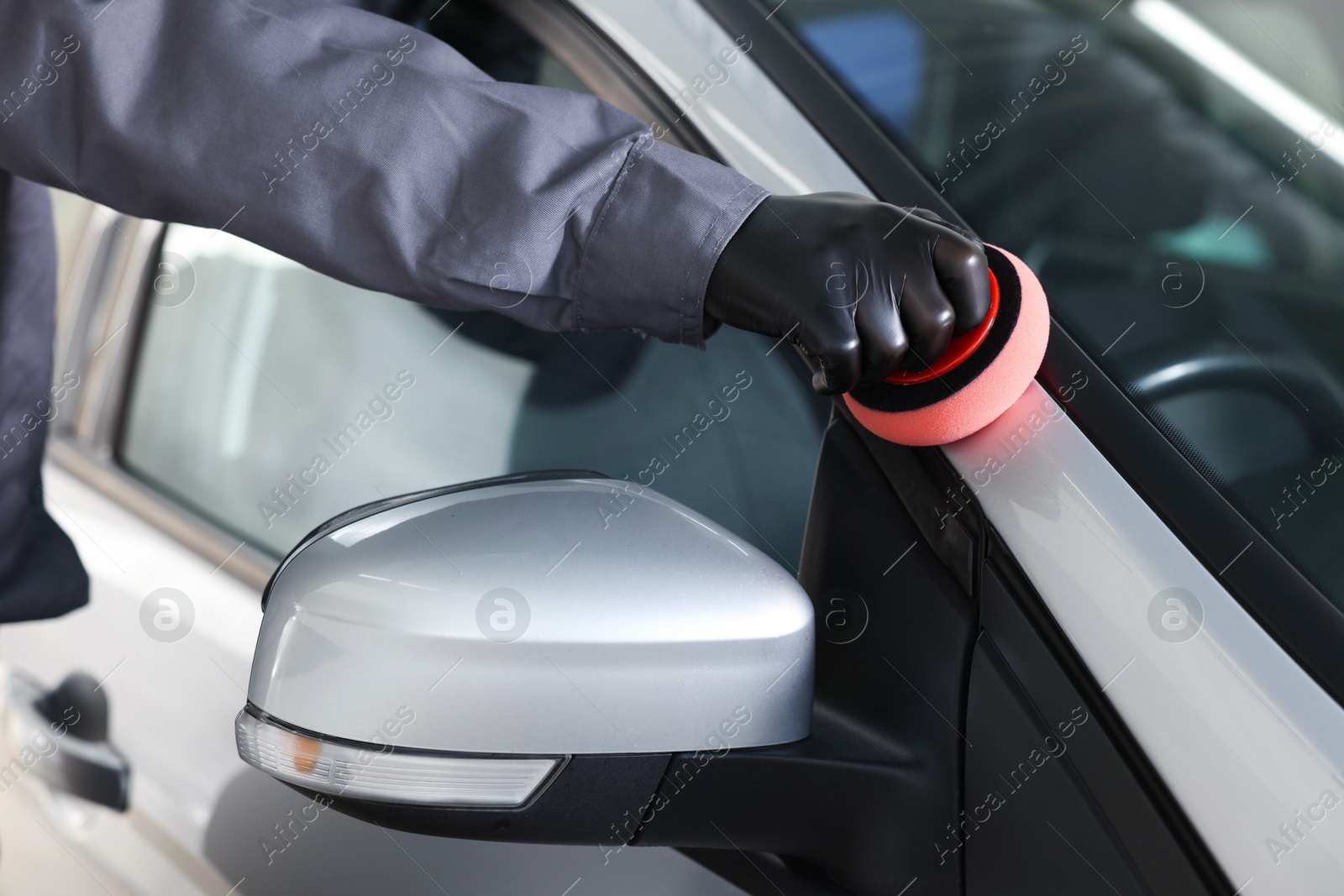 Photo of Man polishing car with sponge indoors, closeup