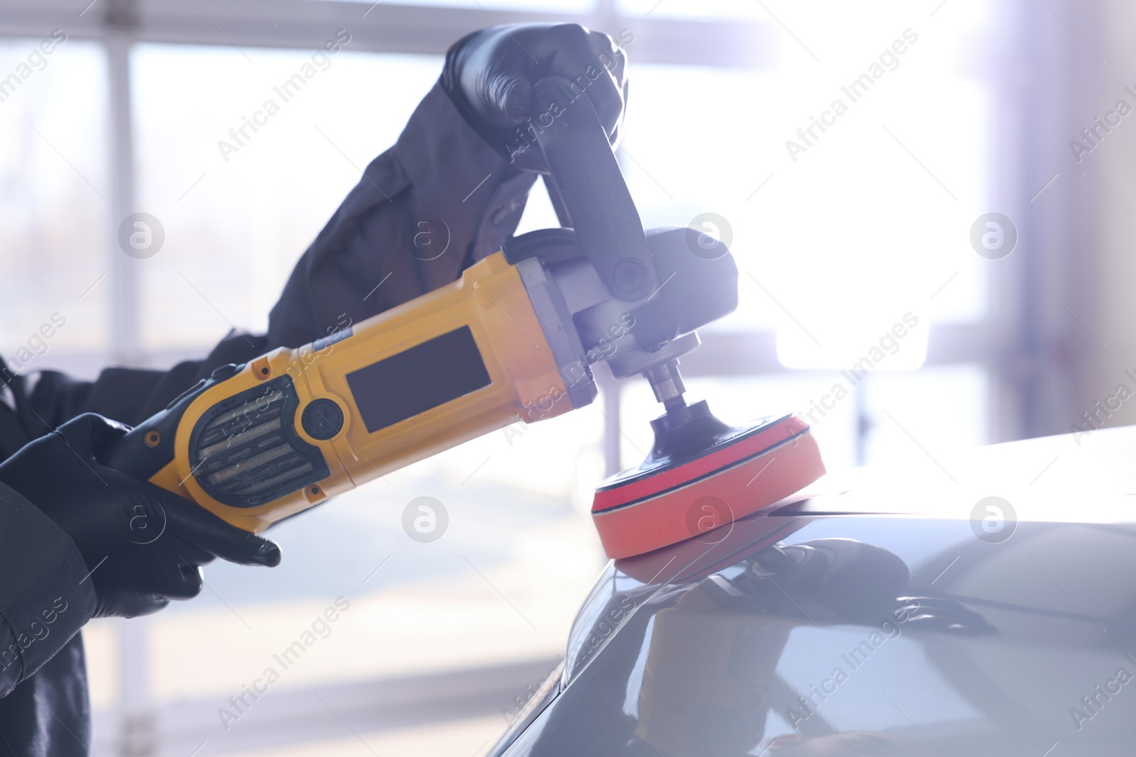 Photo of Man polishing car with orbital polisher indoors, closeup