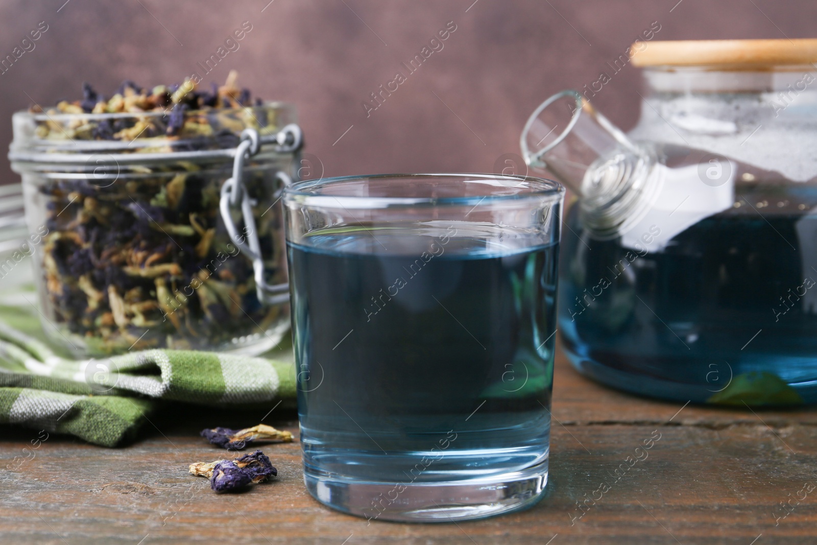 Delicious butterfly pea flower tea on wooden table against brown background Photo of Delicious butterfly pea flower tea on wooden table against brown background