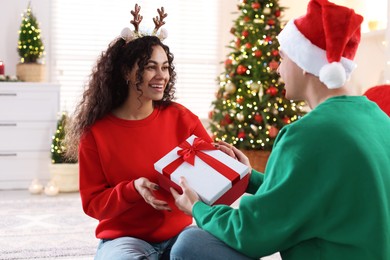 Photo of Young man giving Christmas gift to his happy girlfriend at home