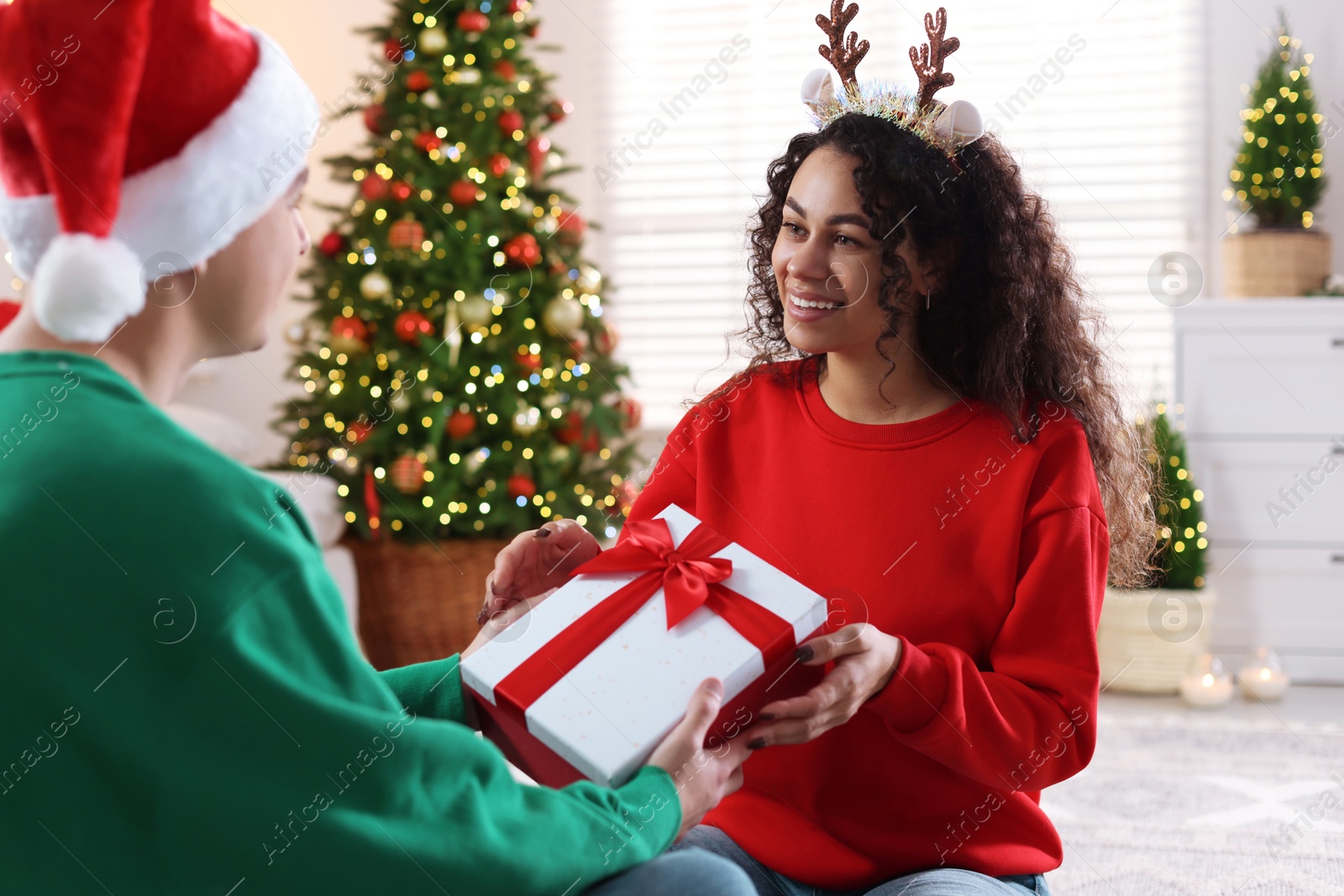 Photo of Young man giving Christmas gift to his happy girlfriend at home