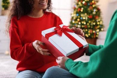 Photo of Young man giving Christmas gift to his happy girlfriend at home, closeup