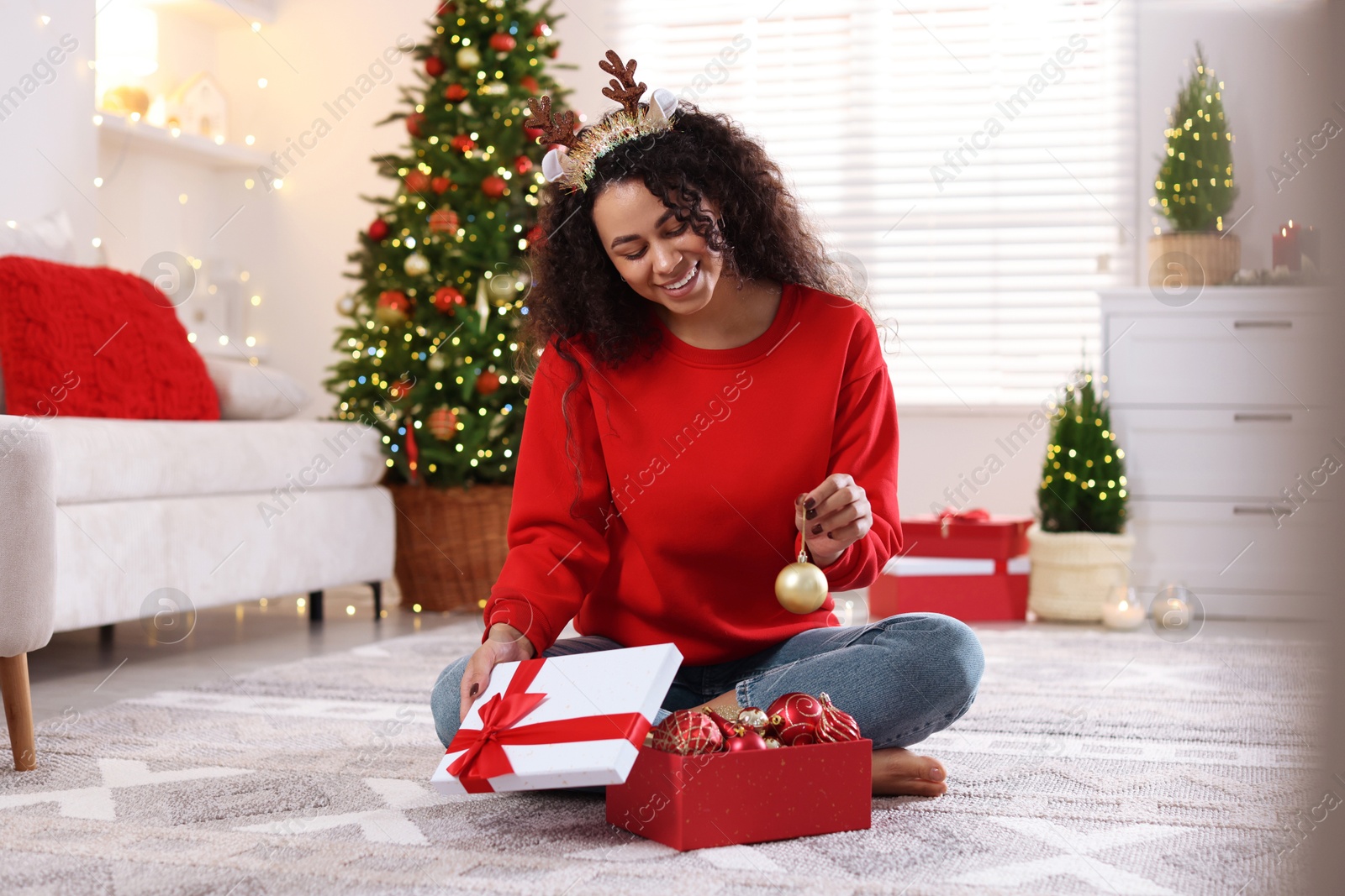 Photo of Happy young woman in reindeer headband with Christmas gift at home