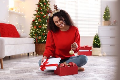 Photo of Happy young woman in reindeer headband with Christmas gift at home