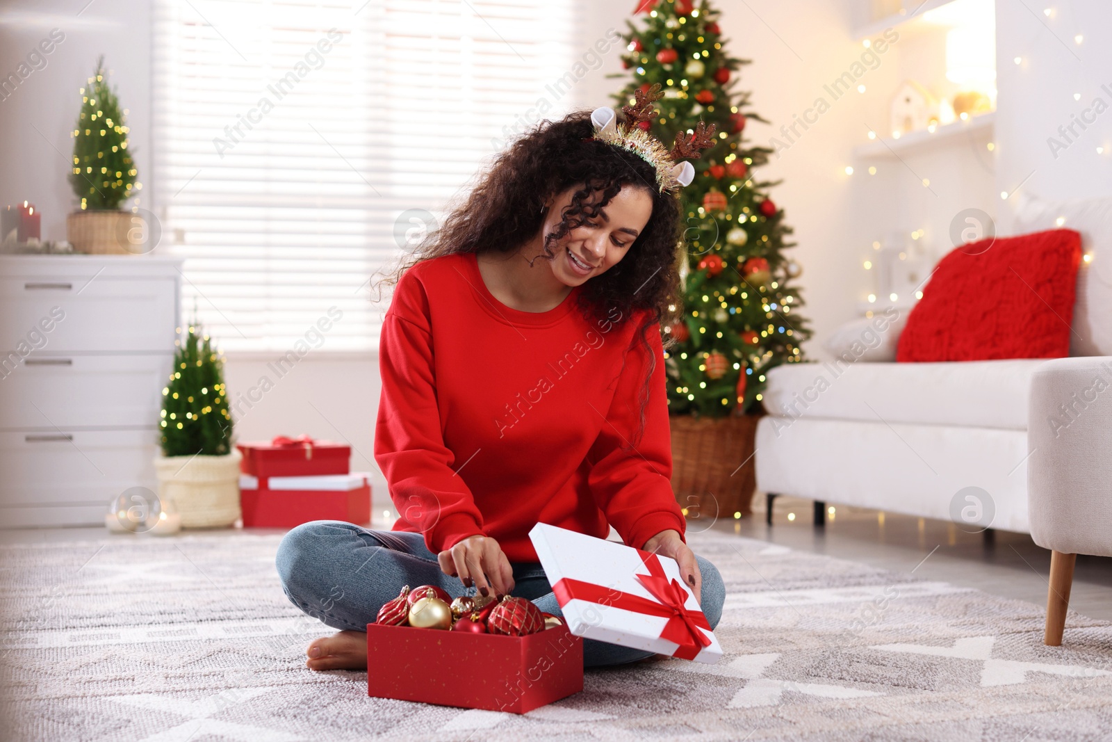 Photo of Happy young woman in reindeer headband with Christmas gift at home