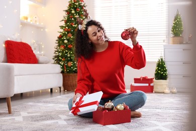 Photo of Happy young woman in reindeer headband with Christmas gift at home