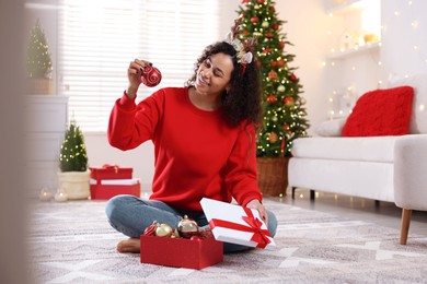 Photo of Happy young woman in reindeer headband with Christmas gift at home